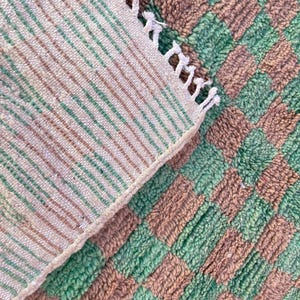 May include: A close-up of a green and brown striped rug with a fringe edge. The rug is made of a soft, fluffy material.