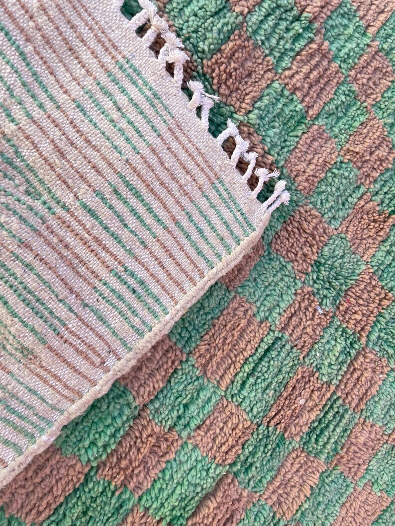 May include: A close-up of a green and brown striped rug with a fringe edge. The rug is made of a soft, fluffy material.