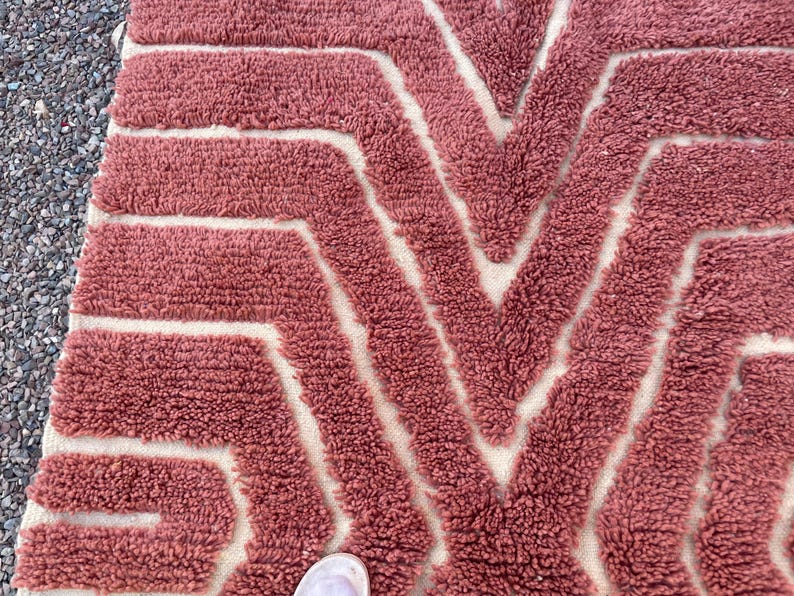 May include: A close-up of a pink and white patterned rug with a geometric design. The rug is made of a soft, fluffy material.