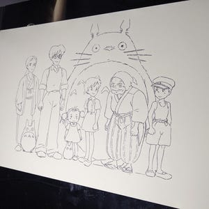 May include: A black and white line drawing of characters from the animated film 'My Neighbor Totoro'. The characters are standing in front of a large, furry creature with big eyes. The creature is Totoro, a friendly forest spirit.