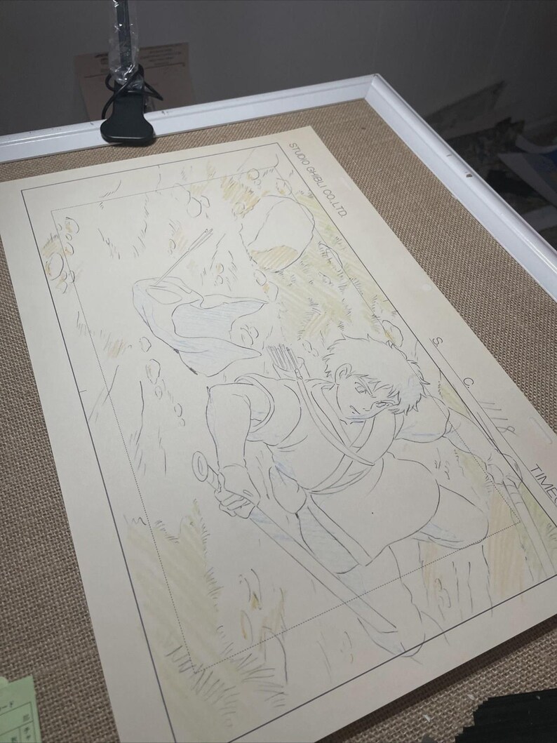 May include: An original animation cel from Studio Ghibli, featuring a detailed sketch of a character with a sword and bow. The artwork is on a beige background, with the text "STUDIO GHIBLI CO.LTD" visible.