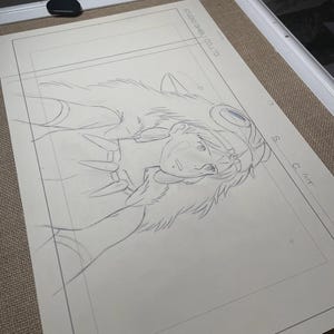 Peut inclure: Un croquis au crayon d'un personnage de Princesse Mononok&eacute; de Studio Ghibli. Le dessin est sur une feuille de papier blanche, encadr&eacute;e dans un cadre blanc. Le texte "STUDIO GHIBLI CO. LTD" est visible.