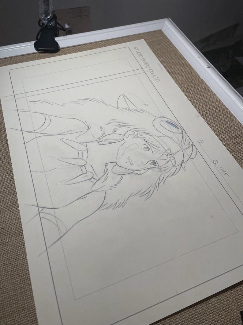 Peut inclure: Un croquis au crayon d'un personnage de Princesse Mononok&eacute; de Studio Ghibli. Le dessin est sur une feuille de papier blanche, encadr&eacute;e dans un cadre blanc. Le texte "STUDIO GHIBLI CO. LTD" est visible.