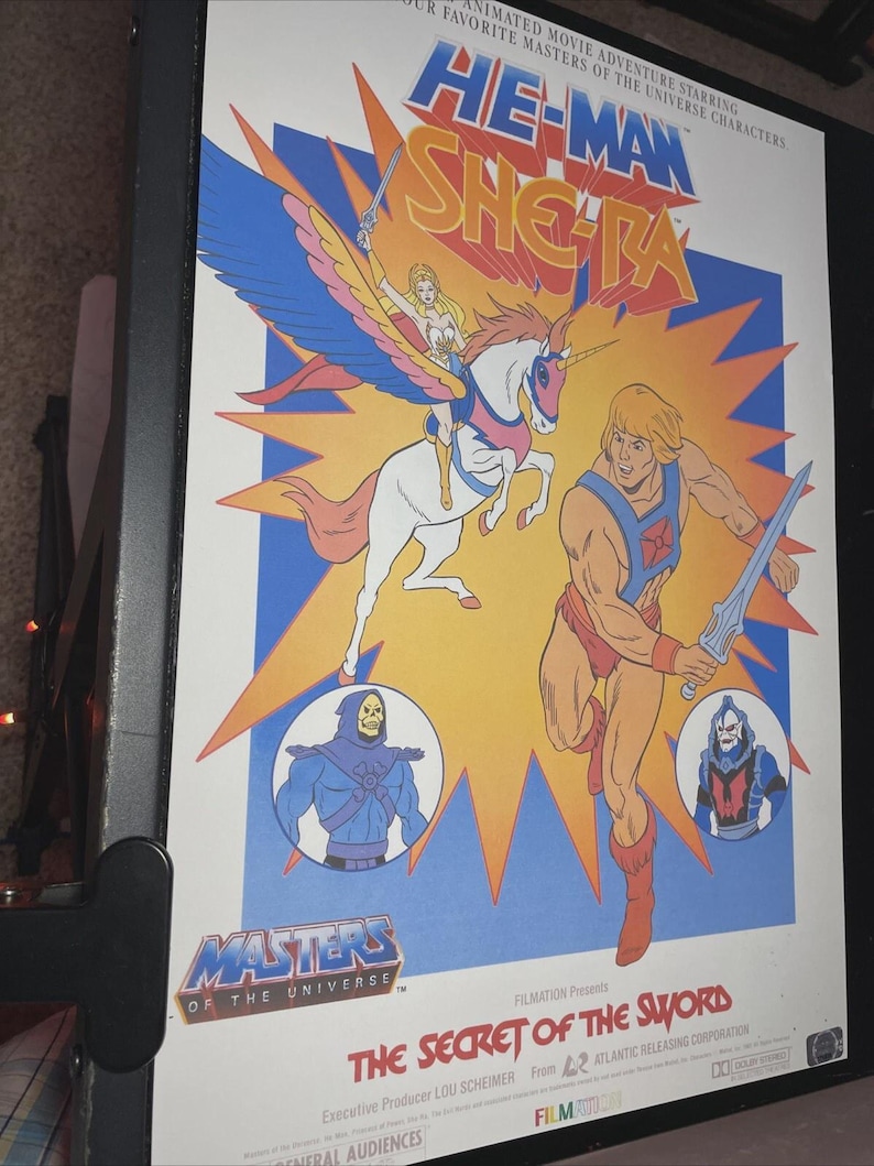 Puede incluir: Un p&oacute;ster enmarcado de la pel&iacute;cula animada "He-Man y She-Ra: El Secreto de la Espada". El p&oacute;ster presenta a He-Man, She-Ra y otros personajes en un dise&ntilde;o colorido y lleno de acci&oacute;n. El t&iacute;tulo se muestra de forma destacada.