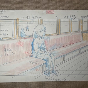 May include: A Studio Ghibli animation cel featuring a young girl seated on a train bench. The cel is hand-drawn with blue, red, and yellow hues. The text "STUDIO GHIBLI" is visible, along with Japanese text and annotations.