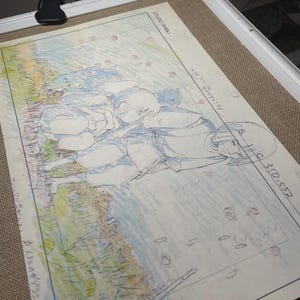 May include: A framed animation cel featuring a hand-drawn scene with two figures lying on the ground. The artwork is in blue and white pencil, with hints of color. The text "STUDIO GHIBLI" is visible in the upper right corner.