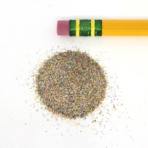 May include: A pile of colorful pencil shavings on a white surface. The shavings are a mix of green, blue, red, yellow, and orange.
