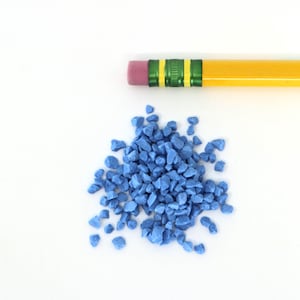Könnte beinhalten: Ein Haufen kleiner, hellblauer, unregelmäßig geformter Steine auf weißem Hintergrund. Ein gelber Bleistift mit einem grünen und rosa Radiergummi befindet sich über den Steinen.