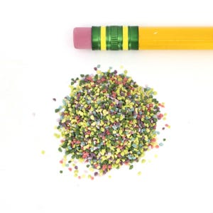 May include: A pile of colorful sprinkles in various shades of green, pink, yellow, and blue. The sprinkles are small and irregular in shape, resembling tiny pebbles.