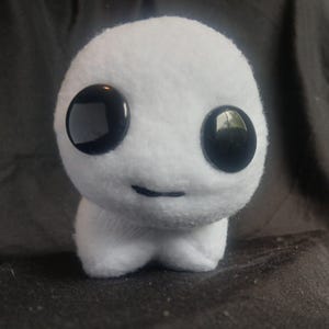 Peut inclure: Jouet en peluche blanc avec de grands yeux noirs et un petit sourire. Le jouet a la forme d'une goutte ronde avec un fond légèrement aplati.