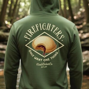 May include: Green hooded sweatshirt with a graphic on the back. The graphic features a pie with a bite taken out, and the words "FIRE FIGHTERS" and "ONLY WANT ONE THING..." are printed above and below the pie. The brand name "Pine&EmberCo" is also printed.