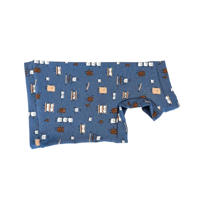 May include: Blue onesie with a repeating pattern of brown and white s'mores. The onesie is made of a soft material and has short sleeves. The s'mores are depicted with graham crackers, marshmallows, and chocolate.