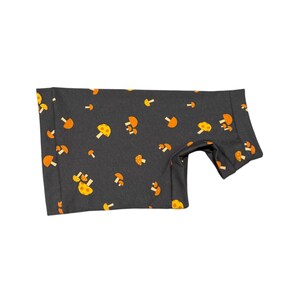 May include: A dark gray garment featuring a repeating pattern of orange and yellow mushrooms. The fabric appears to be soft and the garment is designed to fit a small animal. The mushrooms are in various sizes and orientations.