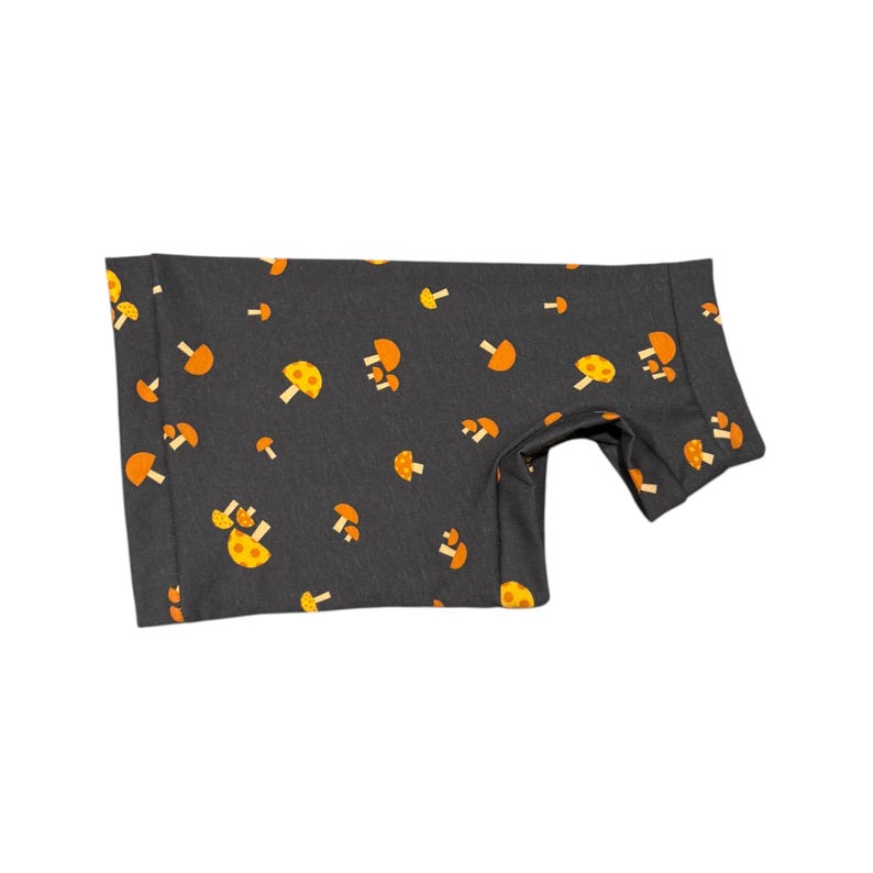 May include: A dark gray garment featuring a repeating pattern of orange and yellow mushrooms. The fabric appears to be soft and the garment is designed to fit a small animal. The mushrooms are in various sizes and orientations.