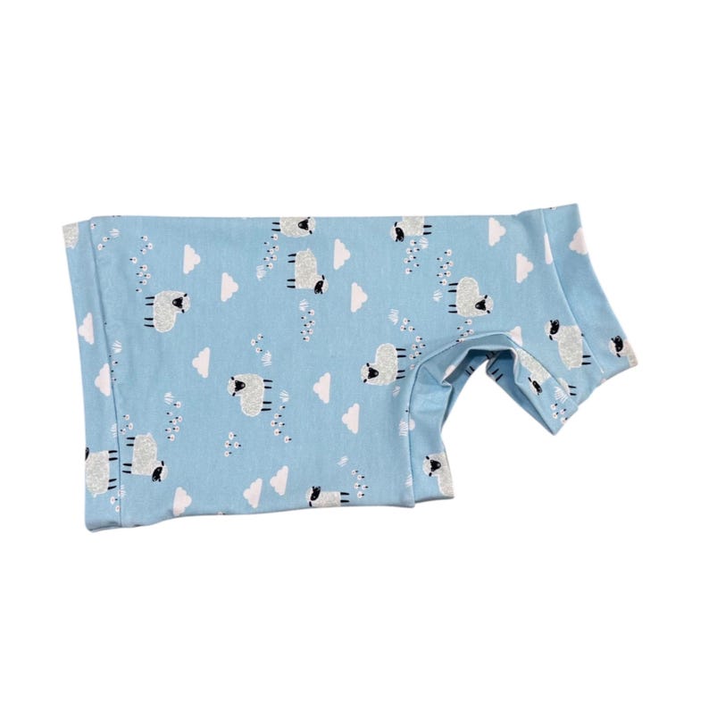 May include: A light blue onesie with a repeating pattern of white sheep and clouds. The onesie has short sleeves and is made of a soft, comfortable material. The garment is designed for babies or toddlers.