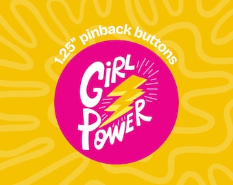 Può includere: Una spilla rotonda rosa con la scritta bianca "GIRL POWER" e un fulmine giallo. Il testo "1.25" pinback buttons" è arcuato sopra il cerchio su uno sfondo giallo con linee ondulate.
