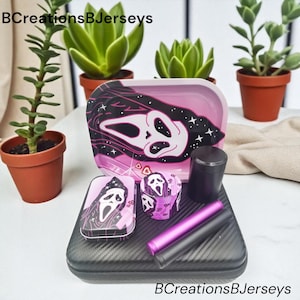 May include: A black and pink rolling tray set with a Scream mask design. The set includes a tray, grinder, storage container, and two cylindrical tools. The text "BCreationsBJerseys" is visible.