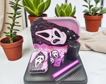 May include: A black and pink rolling tray set featuring a Scream mask design. The set includes a tray, grinder, storage container, and two cylindrical tools. The text "BCreationsBJerseys" is visible.