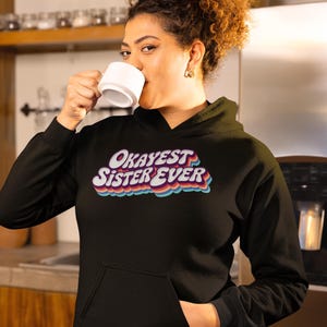 Camiseta o sudadera retro con la hermana más buena del mundo. Regalo divertido para reunión familiar con letras arcoíris de los años 70 y tipografía vintage.
