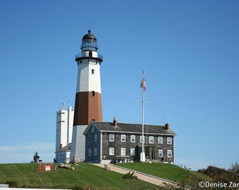 May include: A white and red lighthouse with a black lantern room and a black and white striped tower. The lighthouse is on a grassy hill with a small building in front of it. An American flag is flying on a pole in front of the building.