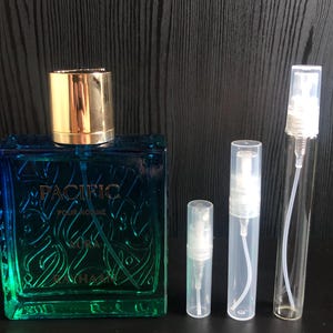 May include: A square blue and green perfume bottle with a gold cap, labeled "PACIFIC POUR HOMME". Several clear, empty spray bottles of varying sizes are next to the perfume bottle.