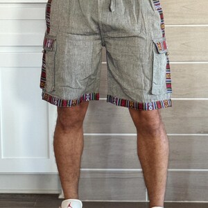 May include: Gray cargo shorts with a drawstring waist and colorful patterned trim along the sides and bottom hem. The shorts have two side pockets and are made of a textured fabric.