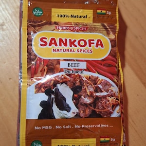 Puede incluir: Dos paquetes de condimento para carne de res Sankofa Natural Spices. Los paquetes son amarillos y marrones con una imagen de una vaca y un plato de carne de res. El texto en el paquete dice "100% Natural" y "Sin MSG. Sin sal. Sin conservantes..."