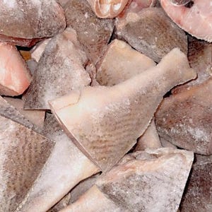 May include: A pile of frozen fish fillets and steaks. The fish pieces vary in size and shape, with a light pinkish-white flesh and a frosted, icy exterior. The image is a close-up, showing the texture and detail of the frozen seafood.