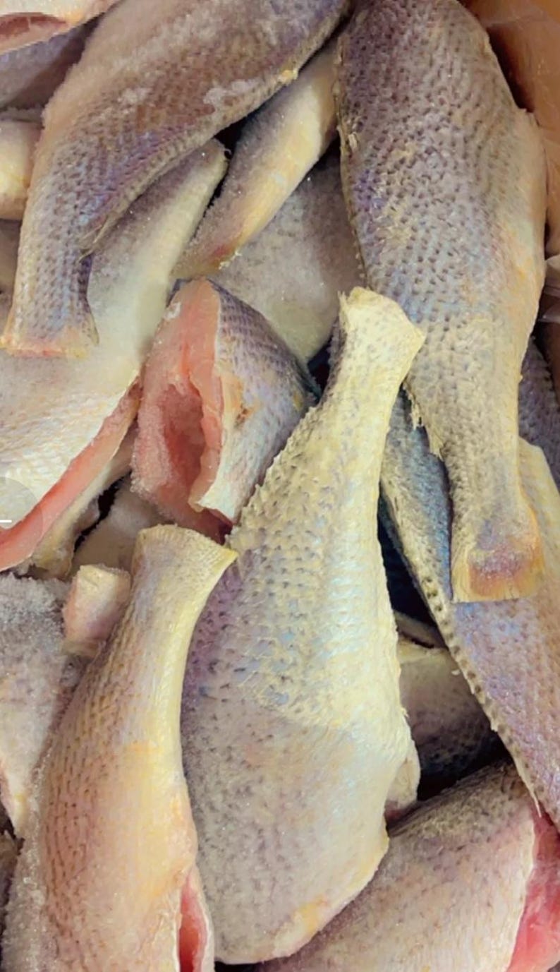 May include: A close-up shot of several raw fish fillets. The fish have a light-colored, textured skin with a hint of blue and pink flesh visible. The fillets are arranged in a pile, suggesting a seafood market or preparation.