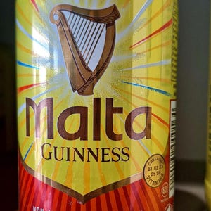 May include: A yellow Malta Guinness can with a brown harp logo. The can features the words "Malta" and "Guinness" in large letters. The bottom of the can has a red and orange design and text that reads "Non-Alcoholic Malt Drink". The can contains 330ml.