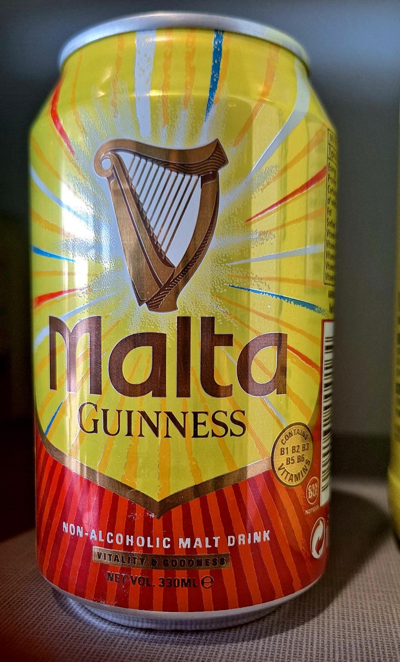 May include: A yellow Malta Guinness can with a brown harp logo. The can features the words "Malta" and "Guinness" in large letters. The bottom of the can has a red and orange design and text that reads "Non-Alcoholic Malt Drink". The can contains 330ml.