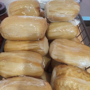 以下が含まれることがあります： 包まれた食べ物の束がいくつか入ったバスケットのクローズアップ。束は薄くて透き通った素材で包まれており、薄い茶色をしています。