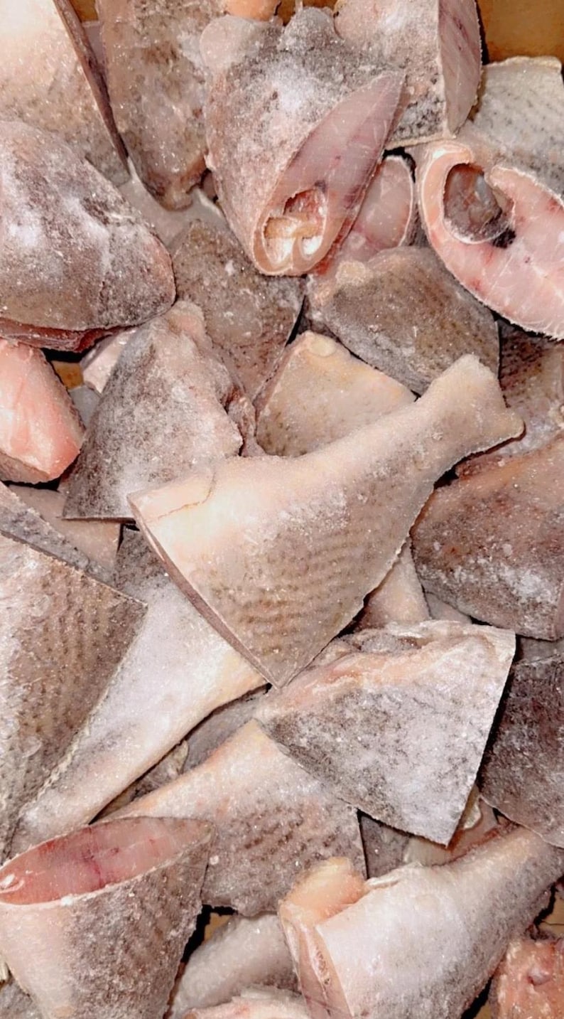 May include: A pile of frozen fish fillets and steaks. The fish pieces vary in size and shape, with a light pinkish-white flesh and a frosted, icy exterior. The image is a close-up, showing the texture and detail of the frozen seafood.