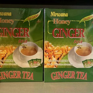 May include: Four green boxes of "Nirwana Honey Ginger Tea" are displayed. Each box features the product name in red and a cup of tea with a honey dipper. The boxes are arranged side by side on a shelf.