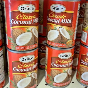 Puede incluir: Una exhibición de latas de leche de coco Grace Classic. Las latas rojas tienen una etiqueta marrón con el nombre de la marca y una ilustración de coco. Cada lata contiene 400 ml de leche de coco.