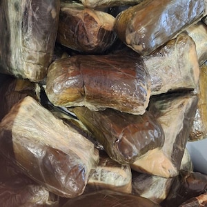 May include: A collection of rectangular, brown packages encased in transparent plastic. The packages have a dark, glossy finish, with some areas appearing lighter. The plastic wrap reflects light, creating highlights.