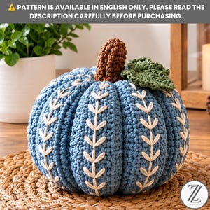 May include: A blue crocheted pumpkin featuring a brown stem, a green leaf, and white embroidered vine patterns along its ribs. The text at the top reads: PATTERN IS AVAILABLE IN ENGLISH ONLY. PLEASE READ THE DESCRIPTION CAREFULLY BEFORE PURCHASING.