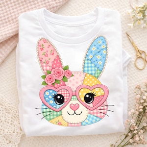 Könnte beinhalten: Weißes T-Shirt mit einem Patchwork-Hasengesicht-Design. Der Hase trägt herzförmige Brillen und hat florale Details. Das Design verwendet rosa, blaue, gelbe und grüne Patches. Ein süßes und farbenfrohes Design, ideal für Ostern oder den Frühling.