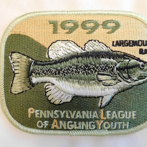 May include: Embroidered patch featuring a largemouth bass. The patch is green, tan, and white, with the text "1999" and "Pennsylvania League of Angling Youth". The fish is detailed with scales and fins.