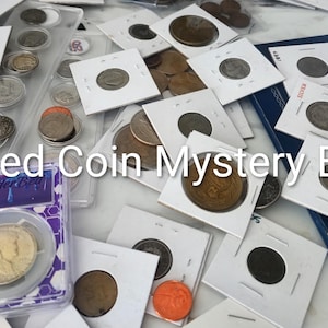 May include: A collection of various coins, some housed in white cardboard holders and others in clear plastic cases, scattered across a surface. The text "Curated Coin Mystery Boxes" is overlaid in white across the center of the image.
