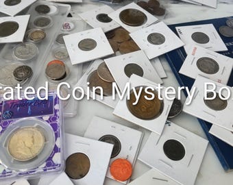 Puede incluir: Una colección de varias monedas, algunas en soportes de cartón blanco y otras en estuches de plástico transparente, esparcidas sobre una superficie. El texto "Curated Coin Mystery Boxes" está superpuesto en blanco sobre la imagen.