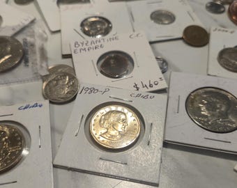 Puede incluir: Una colección de monedas de tonos plateados y dorados en soportes de cartón blanco. Varios soportes presentan texto escrito a mano, incluyendo fechas como 1979-D y 1980-P, y la etiqueta Byzantine Empire. Las monedas muestran retratos y texto.