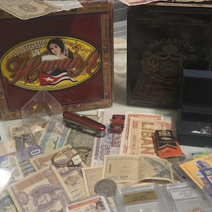 May include: A collection of vintage items including a cigar box with the text "A Night in Havana", a Macanudo cigar box, currency from various countries, a watch, a pocket knife, and a small jewelry box.