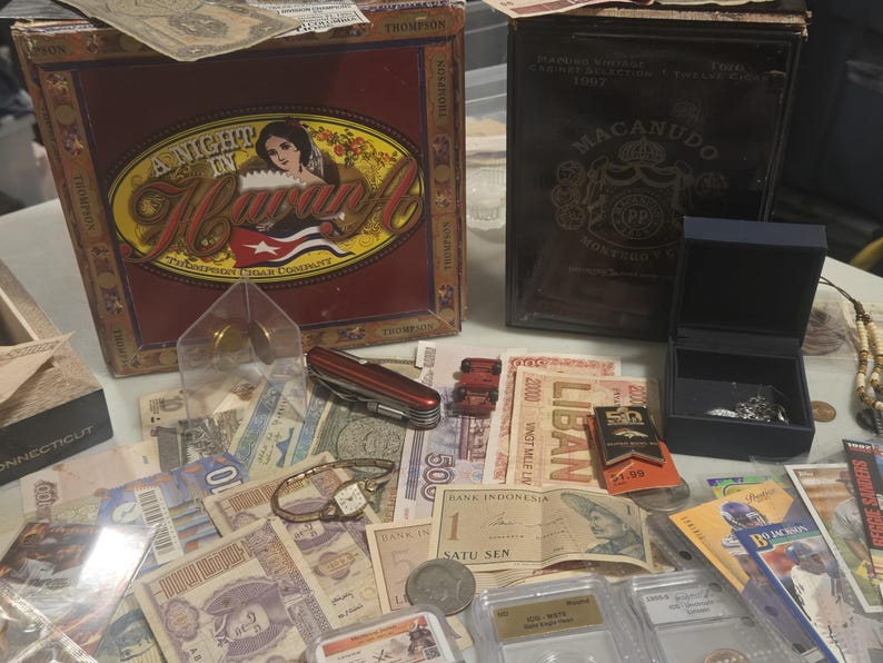 May include: A collection of vintage items including a cigar box with the text "A Night in Havana", a Macanudo cigar box, currency from various countries, a watch, a pocket knife, and a small jewelry box.