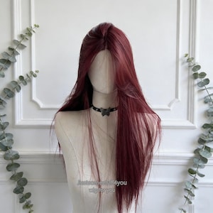 May include: A long, burgundy wig styled on a mannequin. The wig has a natural-looking part and long, flowing layers. A black choker with a butterfly pendant is around the mannequin's neck. The text "Justsomestuff4you wig for you" is visible.