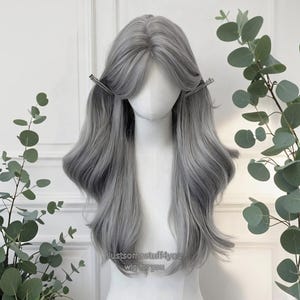 May include: A long, wavy gray wig styled on a mannequin head. The wig features a blend of light and dark gray tones, with bangs and silver hair clips. The text "Justsomestuff4you wig for you" is visible at the bottom.