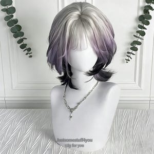 Puede incluir: Una peluca corta sobre una cabeza de maniquí con un estilo en capas. La peluca presenta una mezcla de colores plateado, morado y negro. El texto "Justsomestuff4you wig for you" está en la parte inferior. Un collar plateado con un colgante de llave está alrededor del cuello del maniquí.
