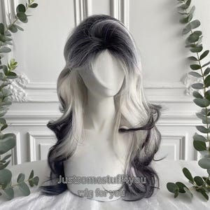 Puede incluir: Una peluca larga y ondulada con una mezcla de tonos negros, grises y blancos. La peluca está peinada con un corte en capas y presenta una raíz oscura que se desvanece en tonos más claros. El texto "Justsomestuff4you wig for you" es visible.