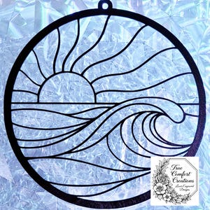 May include: A black, laser-cut wooden wall hanging featuring a sunrise over ocean waves. The design is circular with a small hole at the top for hanging. The image includes the text "True Comfort Creations Laser Engraved Designs."