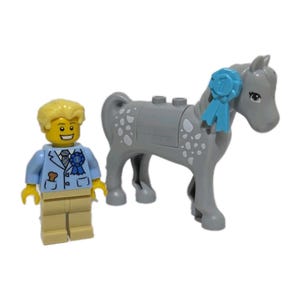 May include: A Lego set with a minifigure and a grey horse. The minifigure wears a light blue jacket, tan trousers, and has yellow hair. The horse has a blue ribbon and white spots. The set is designed for creative play and building.